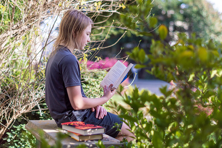 Girl sitting on stone bench and reading books